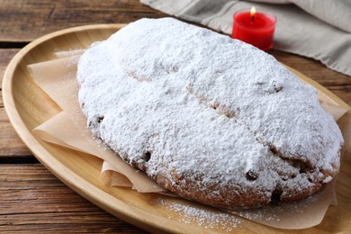 Photo of Wooden plate of delicious Stollen sprinkled with powdered sugar on table, closeup