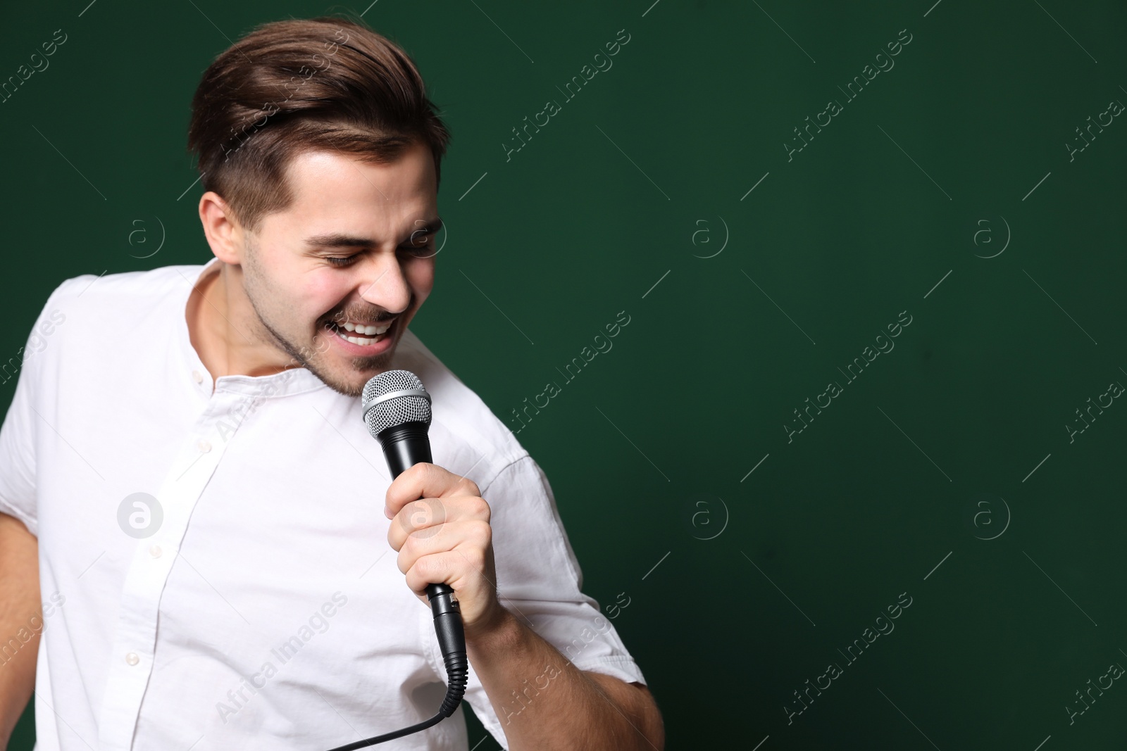 Photo of Young handsome man in casual clothes singing with microphone on color background. Space for text