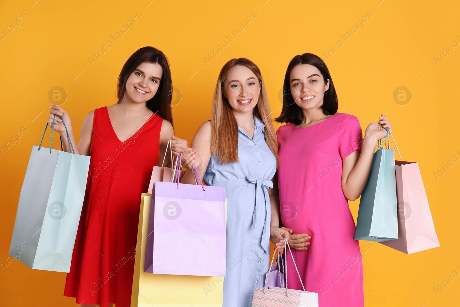 Photo of Happy pregnant women with shopping bags on orange background