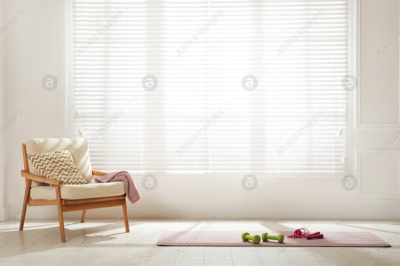 Photo of Exercise mat with dumbbells and jump rope near armchair in spacious room