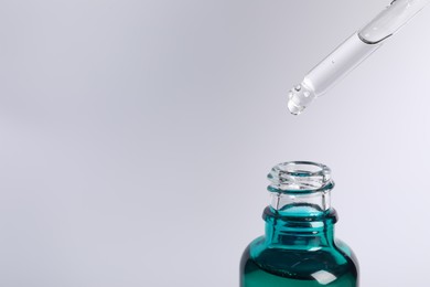 Photo of Dripping cosmetic serum from pipette into bottle on light grey background, space for text