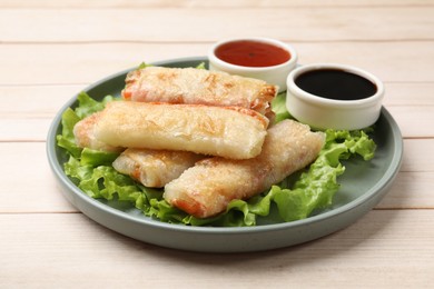 Photo of Delicious fried spring rolls and sauces on light wooden table