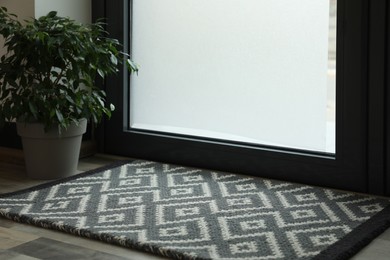 Photo of New clean door mat with pattern and beautiful houseplant on floor near entrance