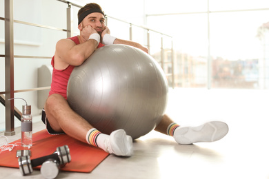 Photo of Lazy young man with sport equipment on yoga mat indoors