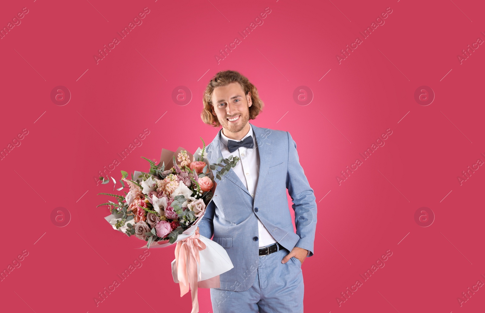 Photo of Young handsome man in stylish suit with beautiful flower bouquet on pink background