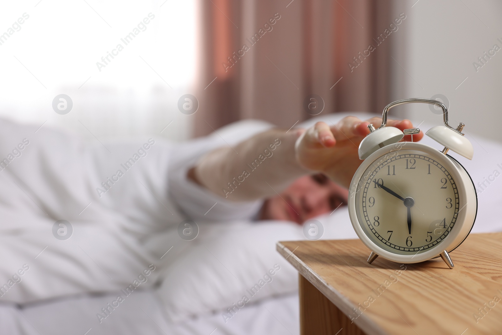 Photo of Man turning off alarm clock in bedroom, focus on hand. Space for text