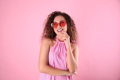 Photo of Young beautiful African-American woman wearing heart shaped glasses on pink background