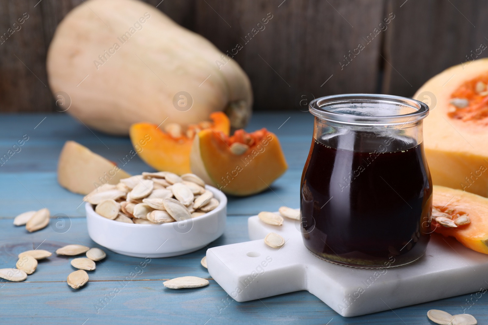 Photo of Fresh pumpkin seed oil in glass jar on blue wooden table