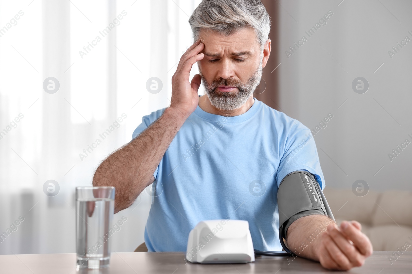 Photo of Man measuring blood pressure at table indoors