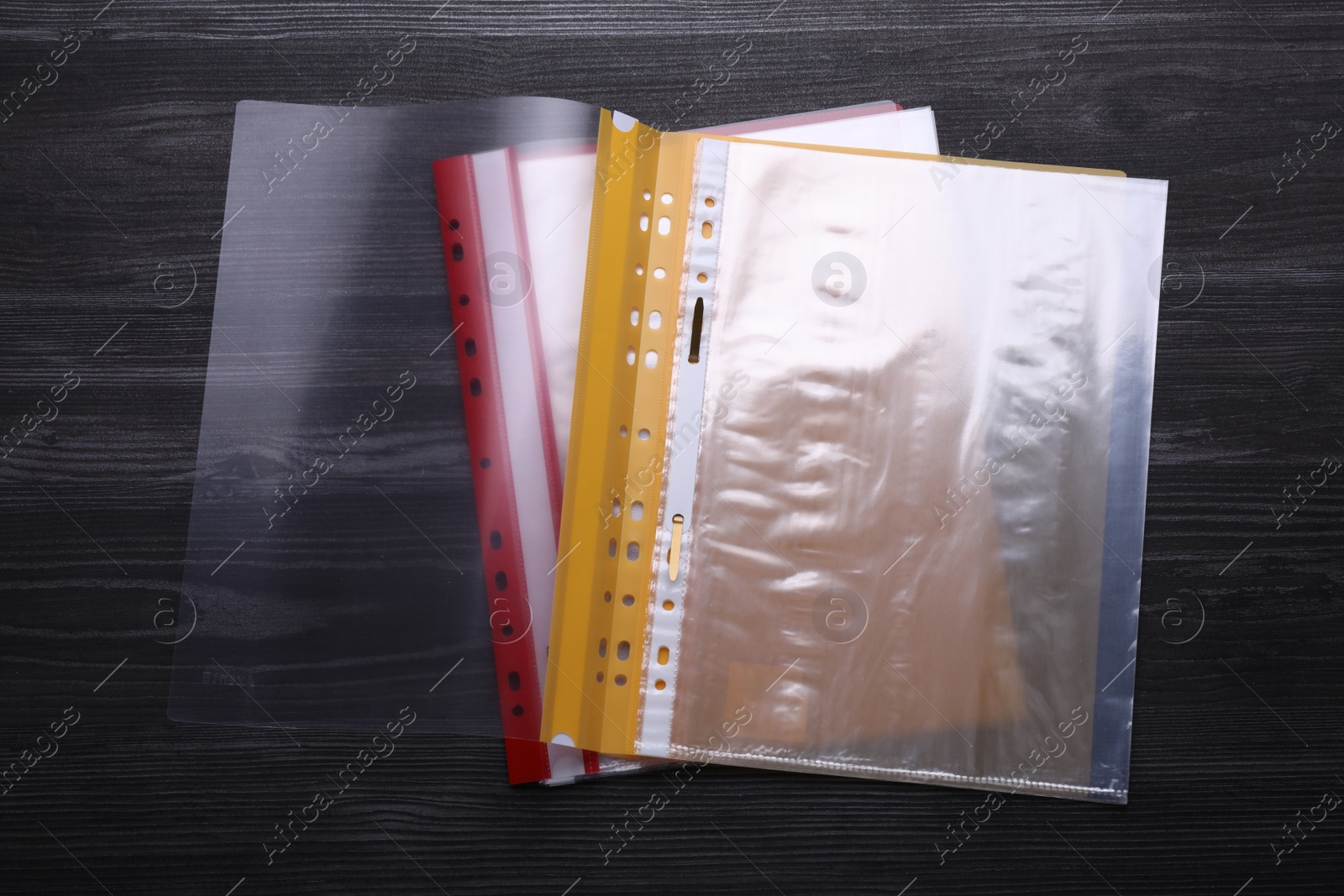 Photo of File folders with punched pockets on black wooden table, flat lay