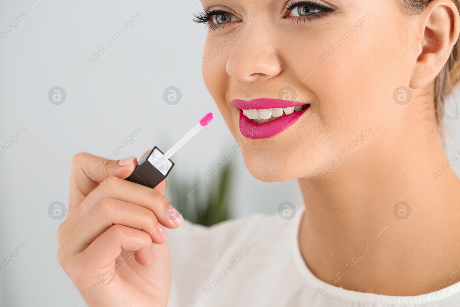 Photo of Beautiful woman applying liquid lipstick on light background