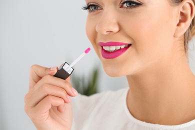 Beautiful woman applying liquid lipstick on light background