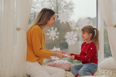 Photo of Happy mother and daughter decorating window with paper snowflakes indoors