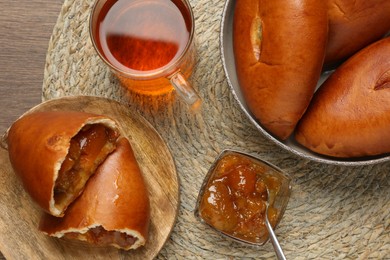 Delicious baked patties with jam and tea on wooden table, top view