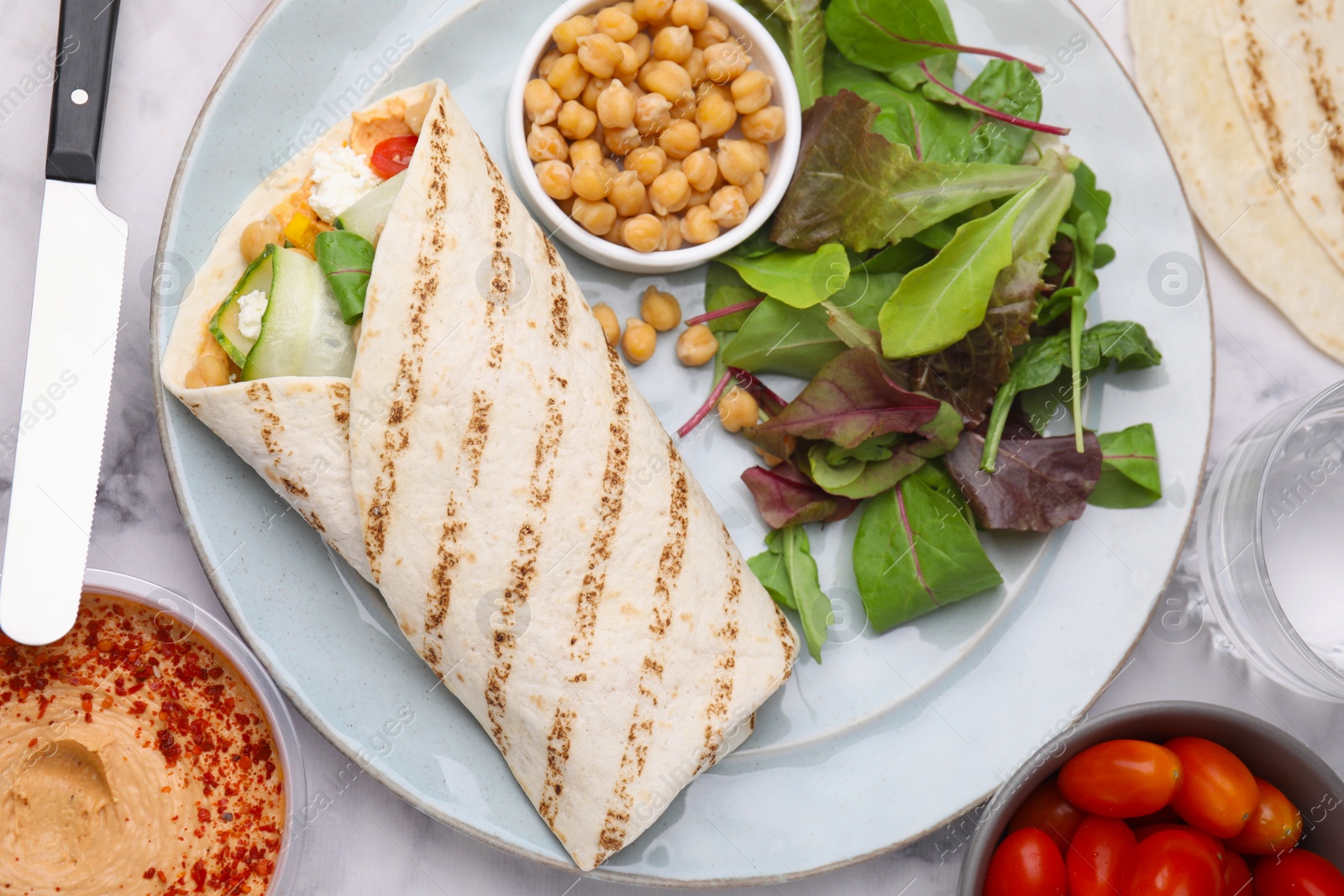 Photo of Plate with hummus wrap and vegetables on white marble table, flat lay