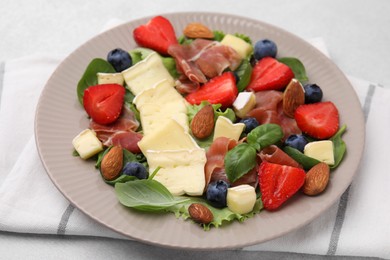 Tasty salad with brie cheese, prosciutto, almonds and berries on table