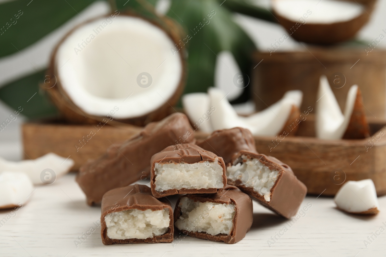 Photo of Delicious milk chocolate candy bars with coconut filling on white wooden table, closeup. Space for text