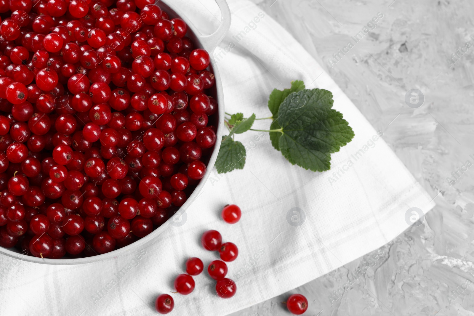 Photo of Ripe red currants in colander and leaves on grey textured table, flat lay. Space for text