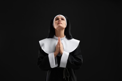 Photo of Nun with clasped hands praying to God on black background