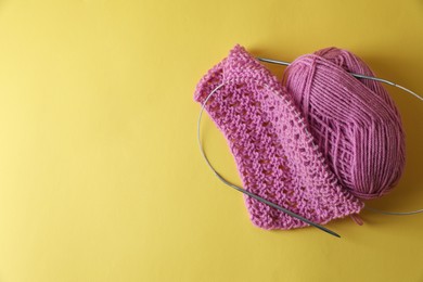 Pink knitting, yarn and needles on yellow background, top view. Space for text