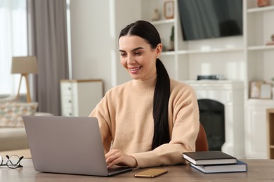 Happy woman working with laptop at wooden desk in room