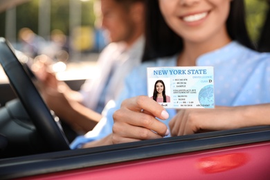 Young woman holding license while sitting in car, closeup. Driving school