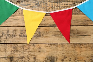 Photo of Bunting with colorful triangular flags on wooden background. Festive decor