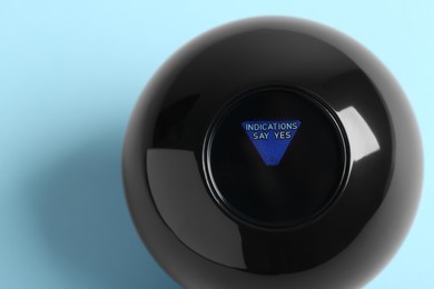 Photo of Magic eight ball with prediction Indications Say Yes on light blue background, top view