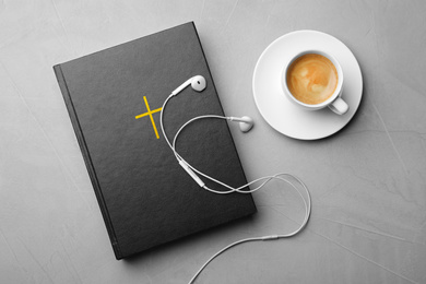 Photo of Bible, cup of coffee and earphones on light grey background, flat lay. Religious audiobook