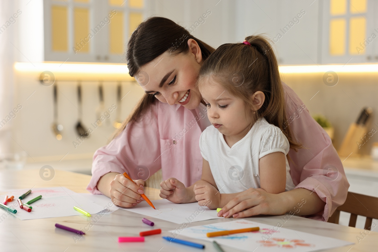 Photo of Mother and her little daughter drawing with colorful markers at table in kitchen