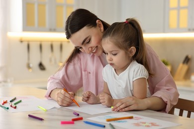 Photo of Mother and her little daughter drawing with colorful markers at table in kitchen