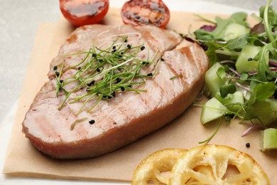 Photo of Delicious tuna steak, salad and lemon on parchment paper, closeup