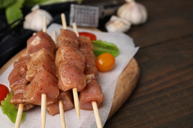 Photo of Skewers with cut raw marinated meat on wooden table, closeup. Space for text