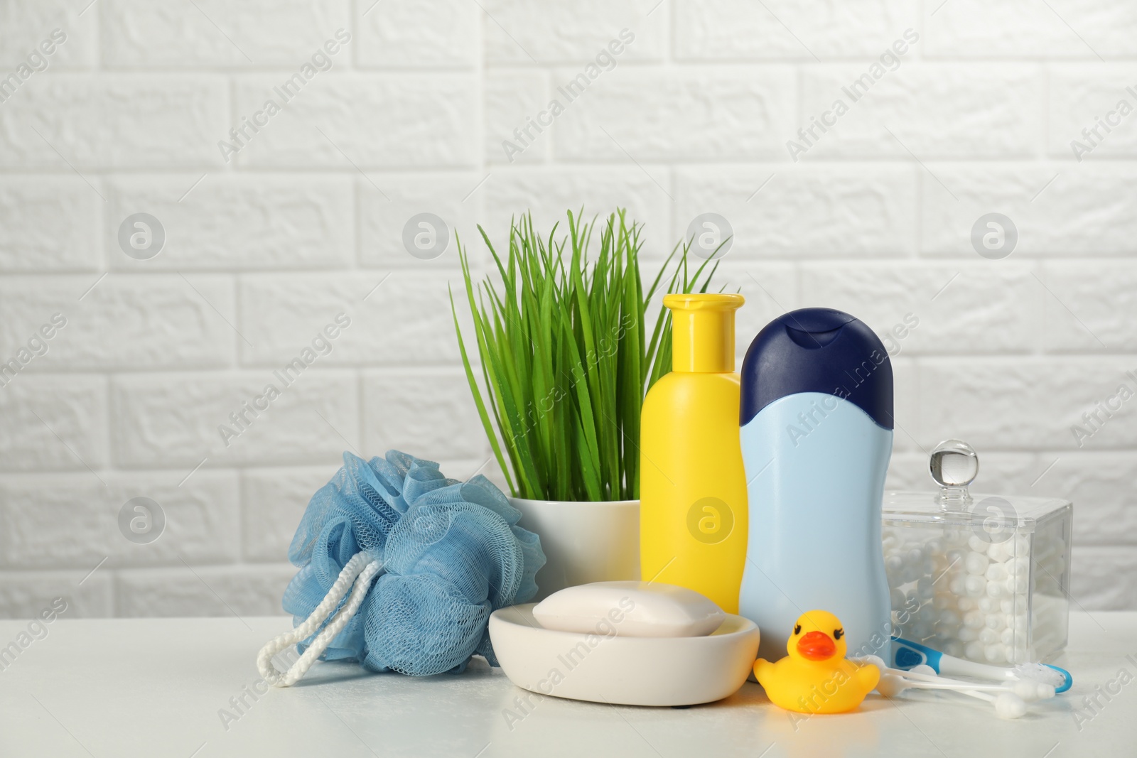 Photo of Different baby bath accessories and cosmetic products on white table against brick wall