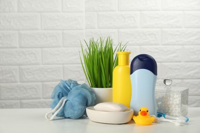 Different baby bath accessories and cosmetic products on white table against brick wall