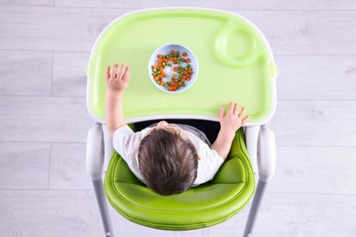 Photo of Cute little baby eating healthy food in high chair indoors, top view