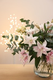 Photo of Bouquet of beautiful lily flowers in vase on table against beige background