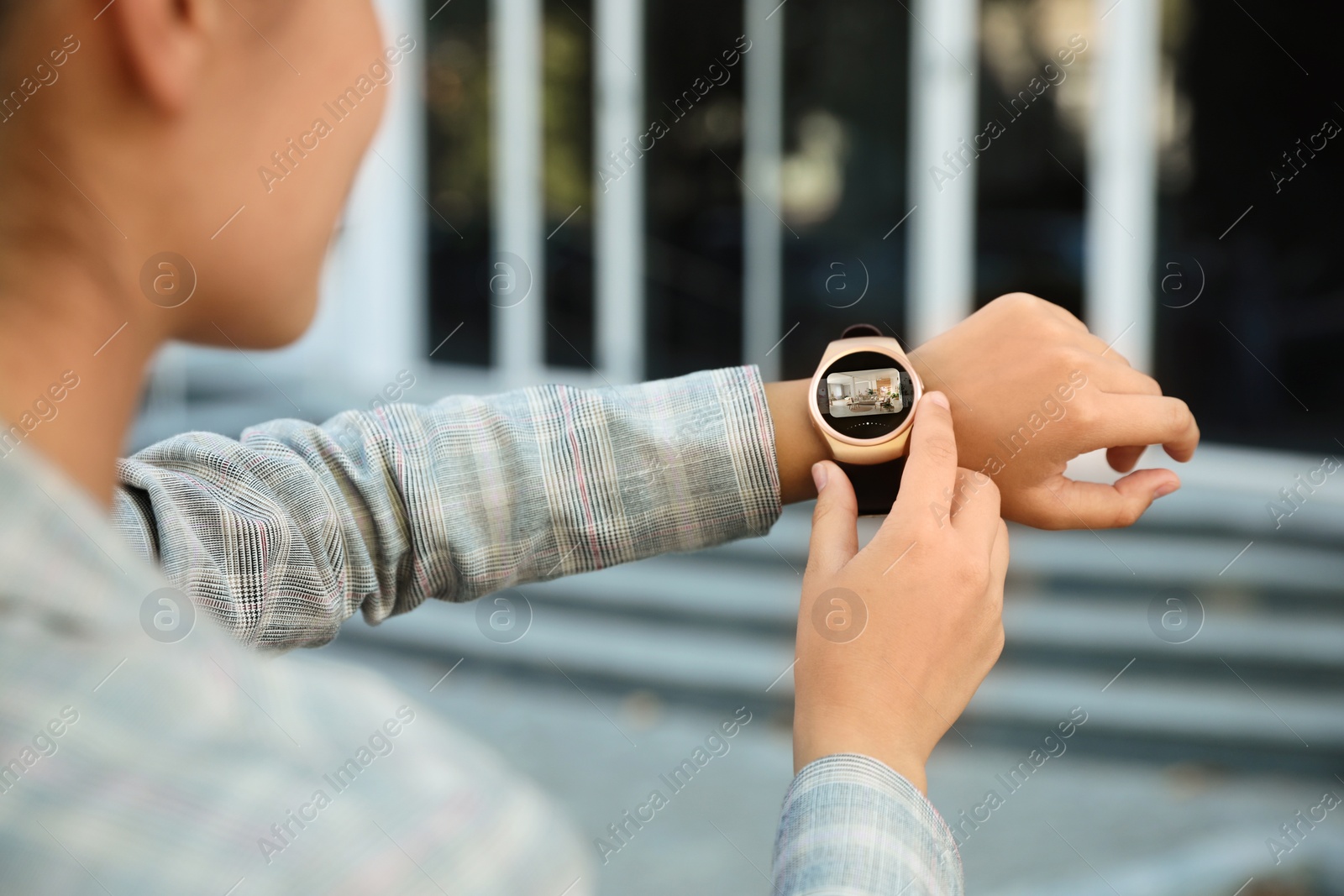 Image of Woman checking home security system via smartwatch app outdoors, closeup.  room through CCTV camera on display