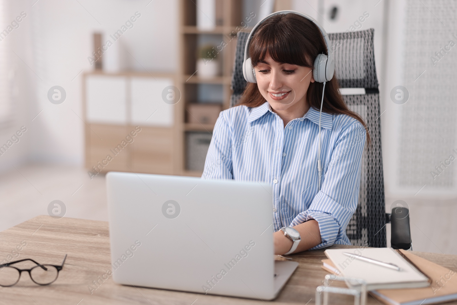 Photo of Woman in headphones watching webinar at wooden table in office