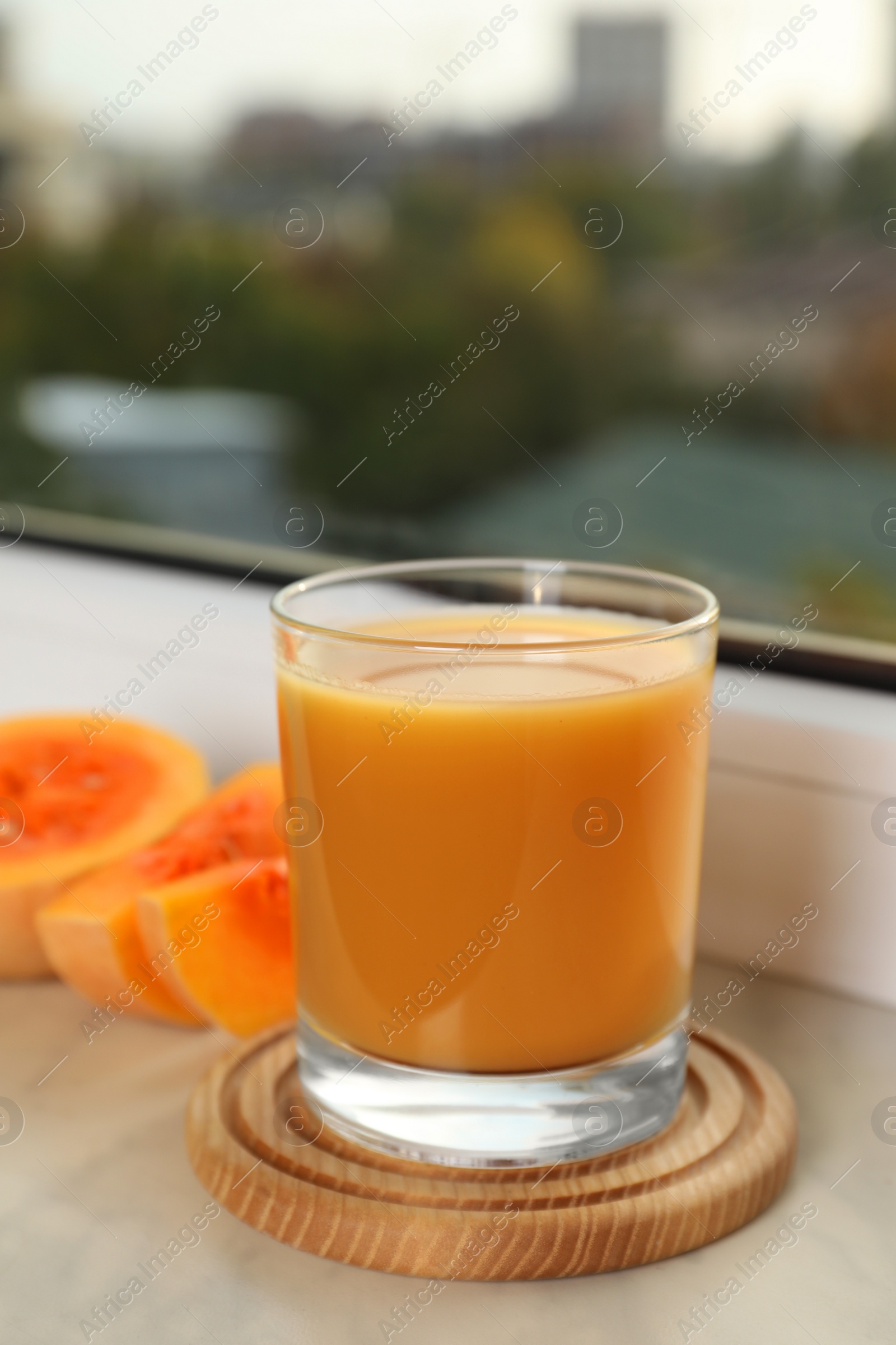 Photo of Tasty pumpkin juice in glass and cut pumpkin on windowsill indoors