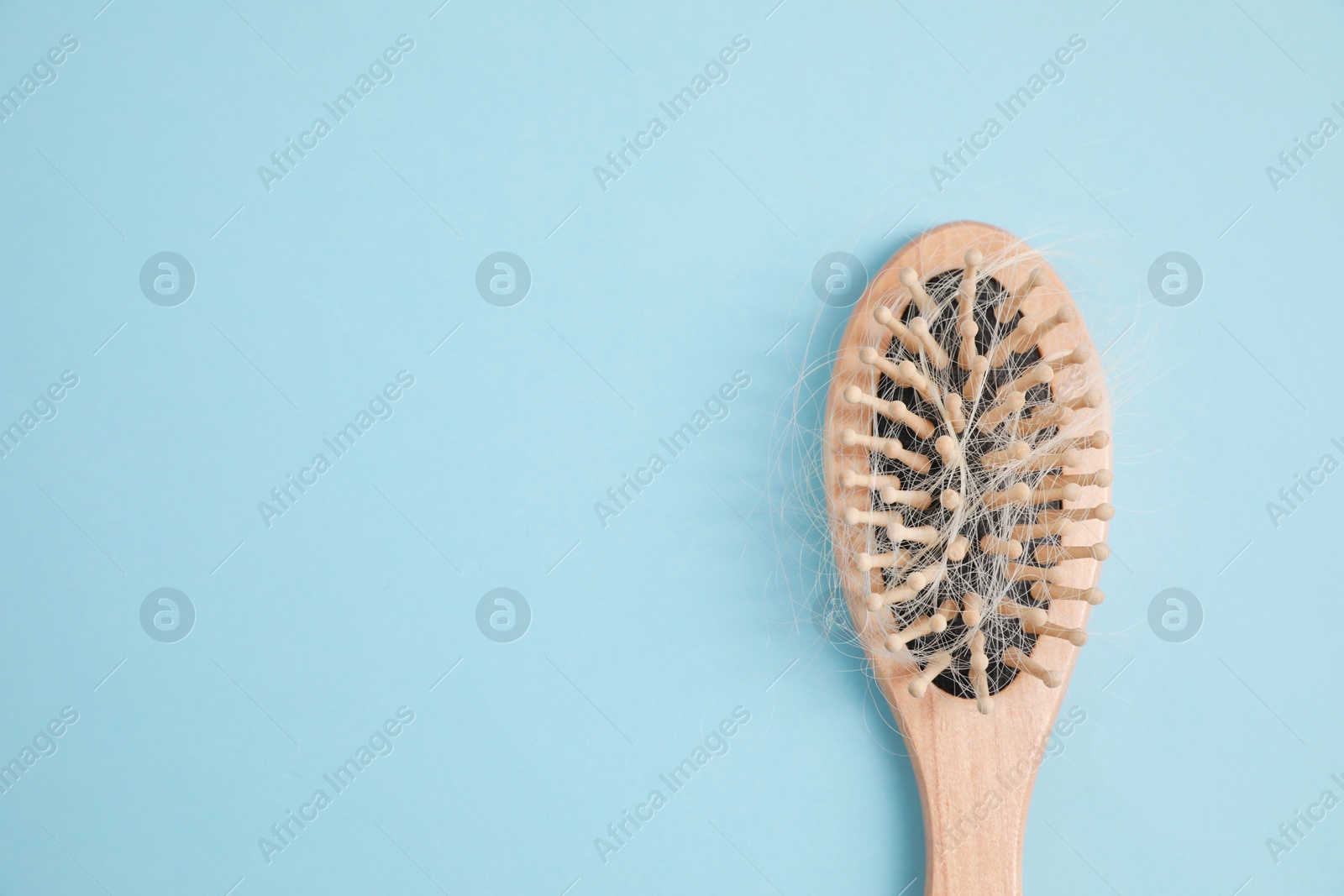 Photo of Wooden brush with lost hair on light blue background, top view. Space for text