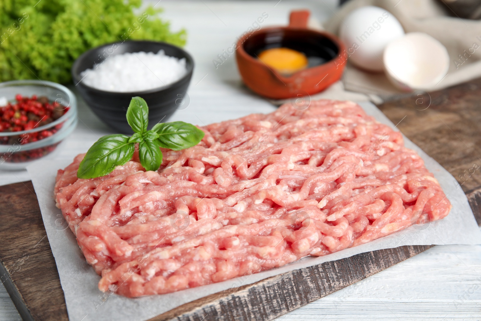 Photo of Raw chicken minced meat with basil on white wooden table, closeup