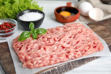 Photo of Raw chicken minced meat with basil on white wooden table, closeup