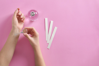 Woman applying perfume on pink background, top view. Space for text