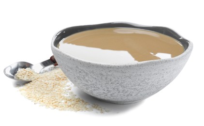 Photo of Tasty sesame paste in bowl, spoon and seeds on white background