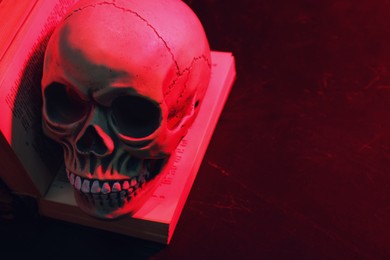 Photo of Human skull and old book in red neon light on table. Space for text