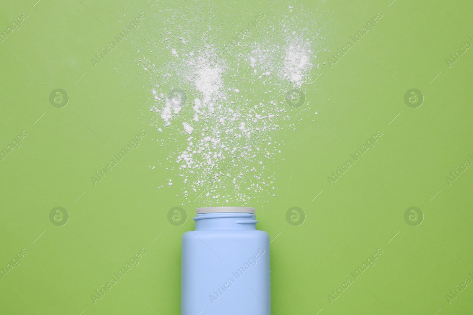 Photo of Bottle and scattered baby powder on green background, top view