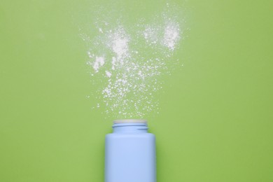 Bottle and scattered baby powder on green background, top view