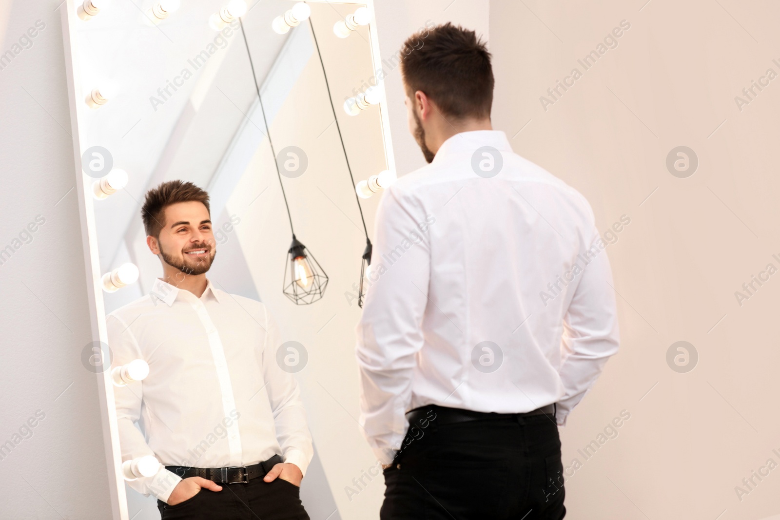 Photo of Young man looking at himself in large mirror at home