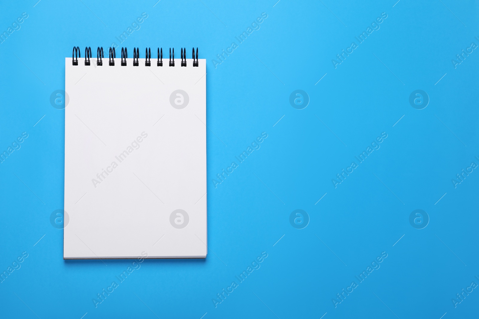 Photo of Open notebook on light blue background, top view. Space for text